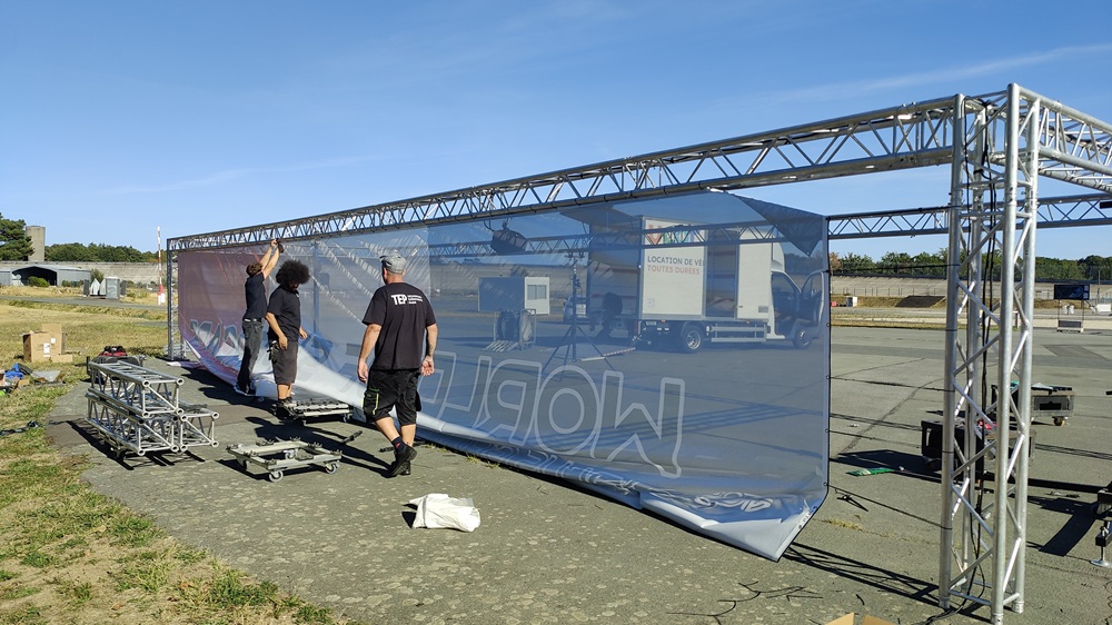 Équipe de techniciens T.E.P. installant une structure autoportée en aluminium et une bâche scénique imprimée